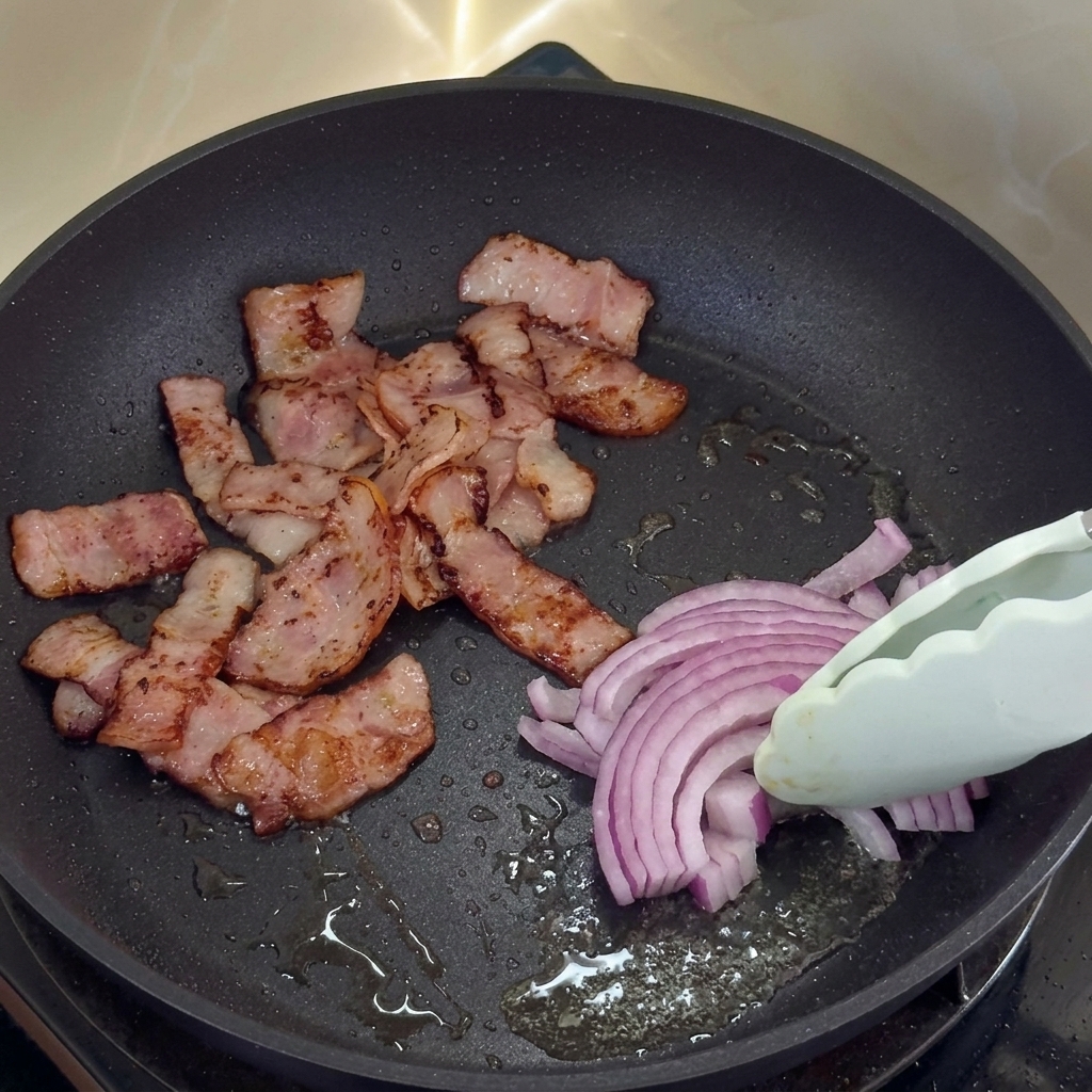 Oignons rouges cuisant dans la graisse de bacon à côté du bacon croustillant.