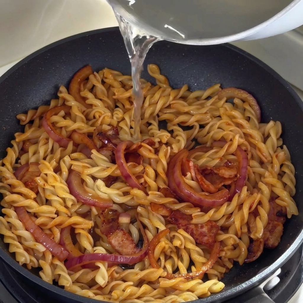Eau de cuisson des pâtes versée dans la poêle contenant les fusilli.