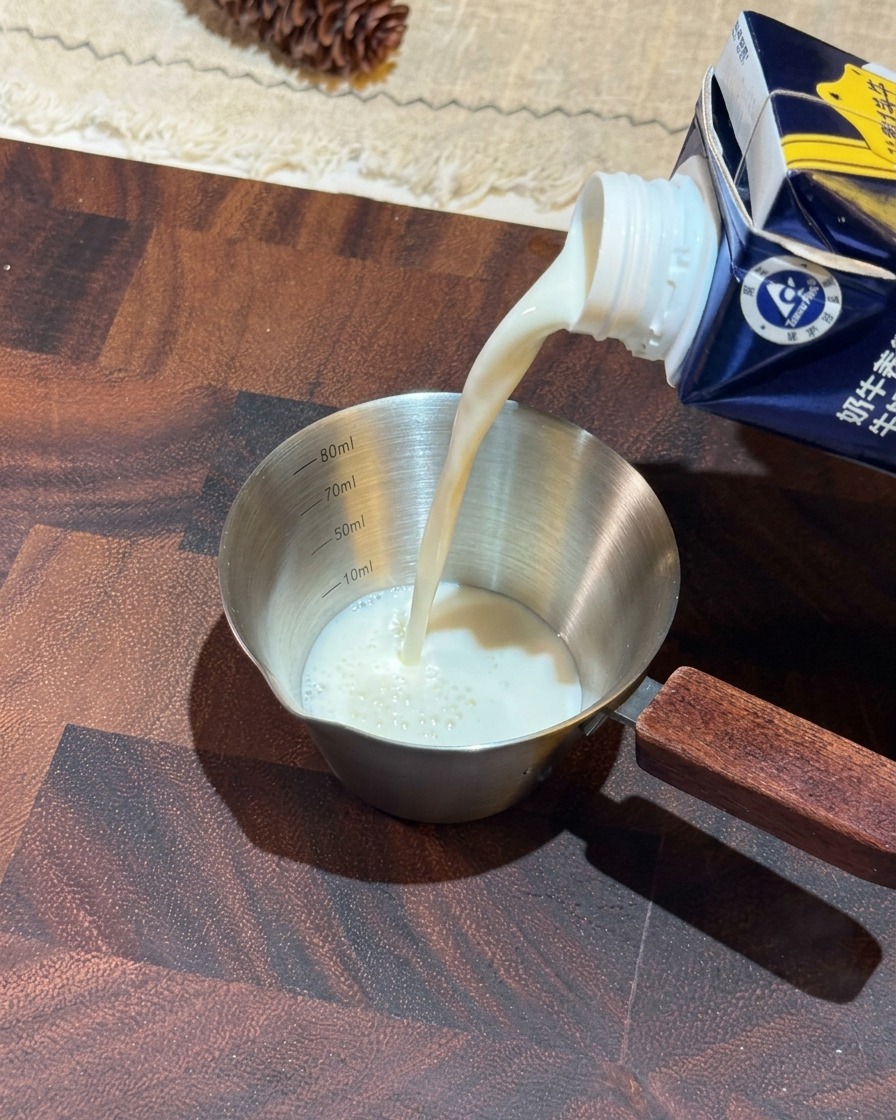 Du lait blanc versé dune brique bleue dans un verre doseur en inox avec une poignée en bois.