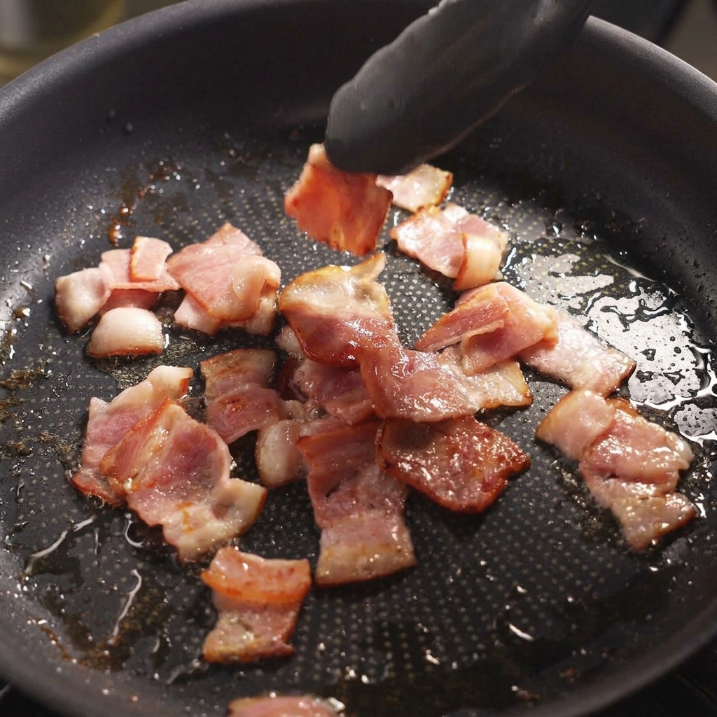 Des pinces retournant des morceaux de bacon grésillants dans une poêle.