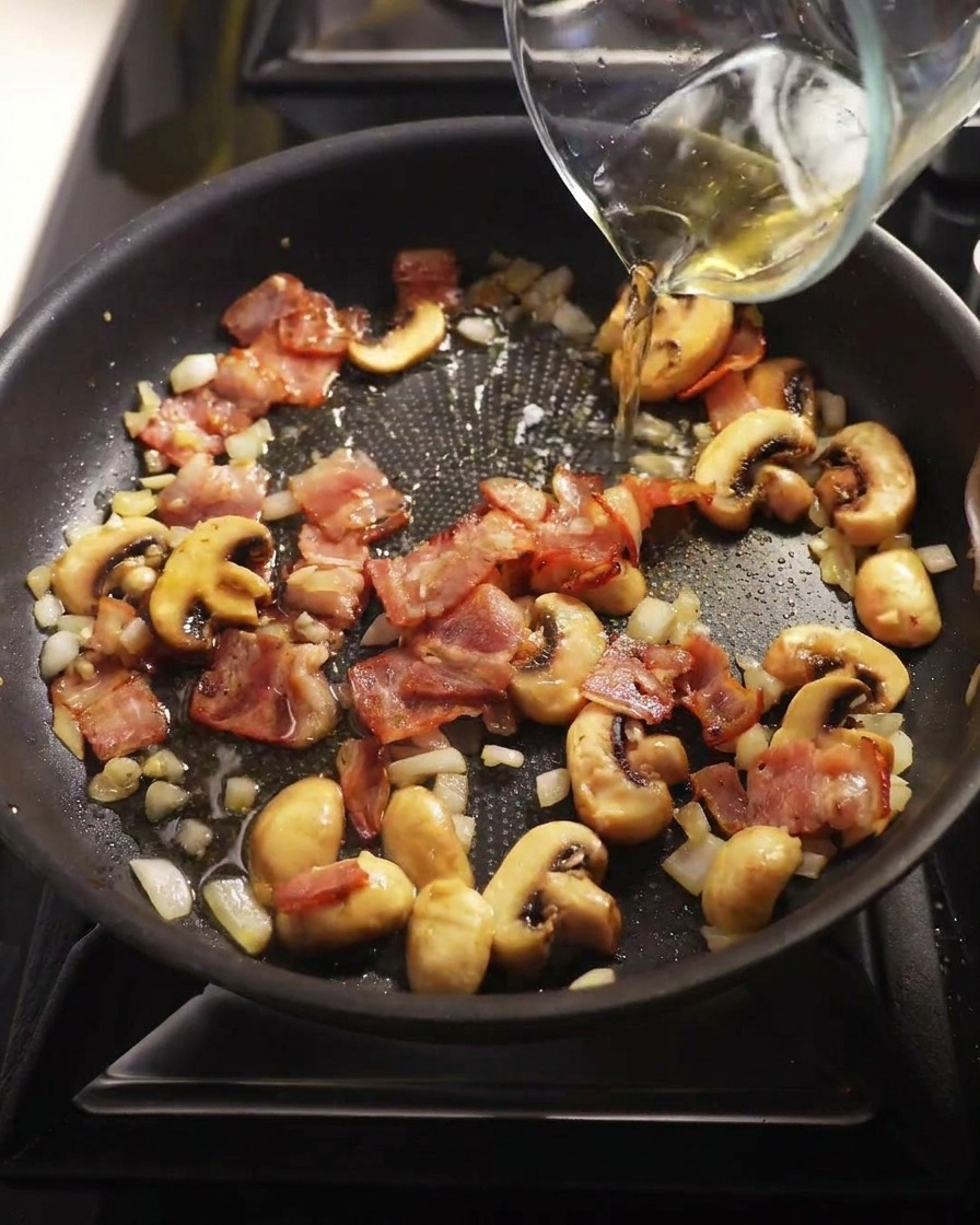 Vin blanc versé dans la poêle contenant les champignons et le bacon.