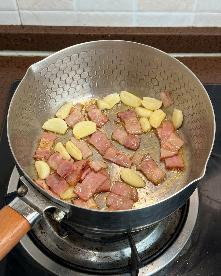 Champignons tranchés, morceaux de bacon et lamelles dail cuisant ensemble dans une poêle.