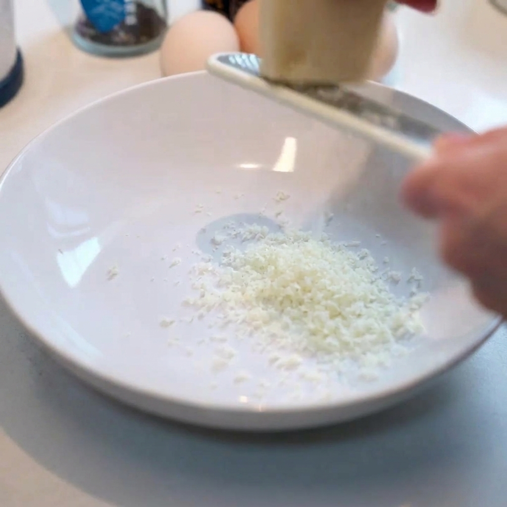 Râpage de parmesan frais dans un bol blanc.