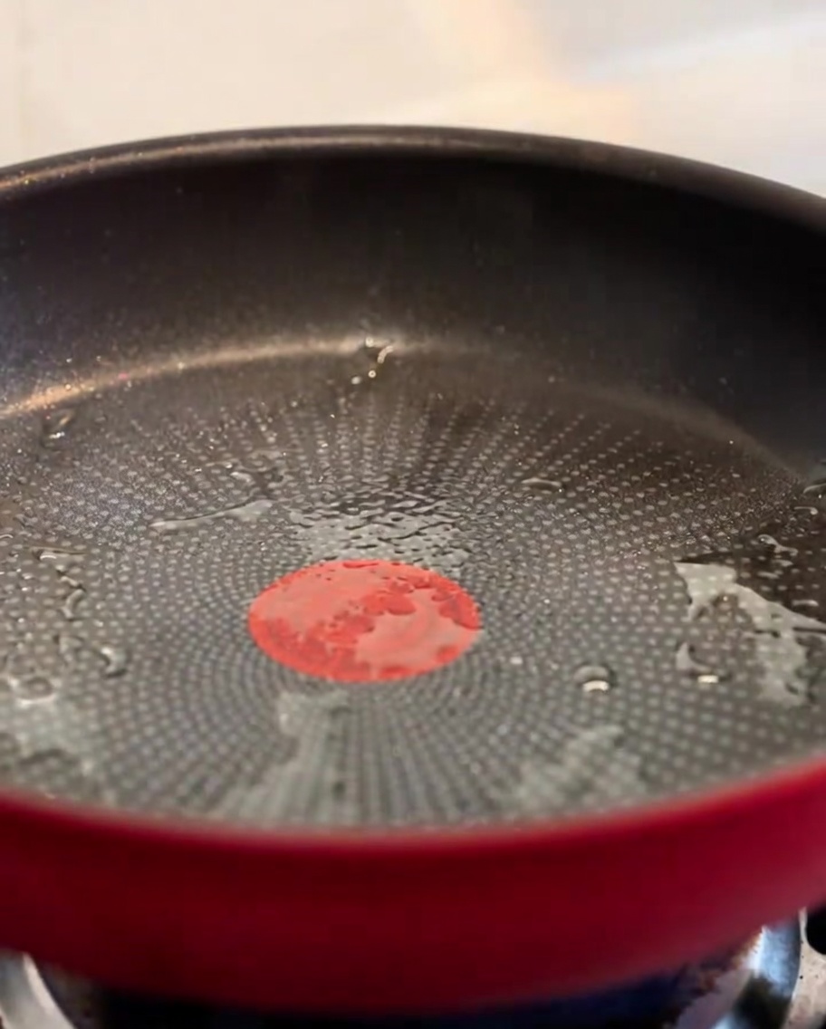 Morceaux de bacon croustillants grésillant dans une poêle rouge.