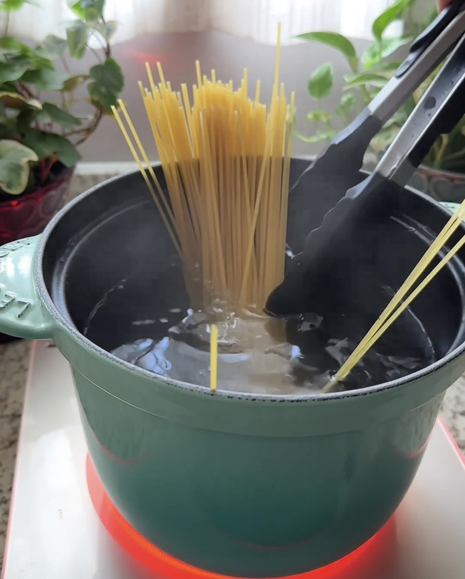 Spaghettis secs plongés dans une casserole turquoise remplie deau bouillante.