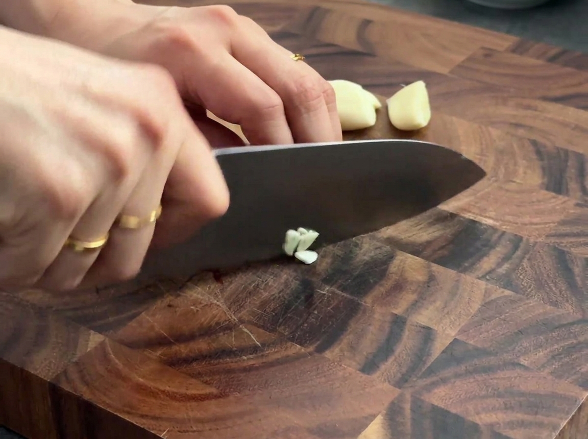 Gousses dail frais hachées sur une planche à découper en bois avec un couteau de chef.