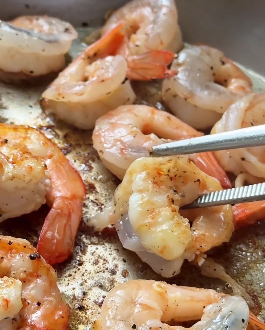 Crevettes saisies dans une poêle chaude avec une coloration dorée sur les bords.