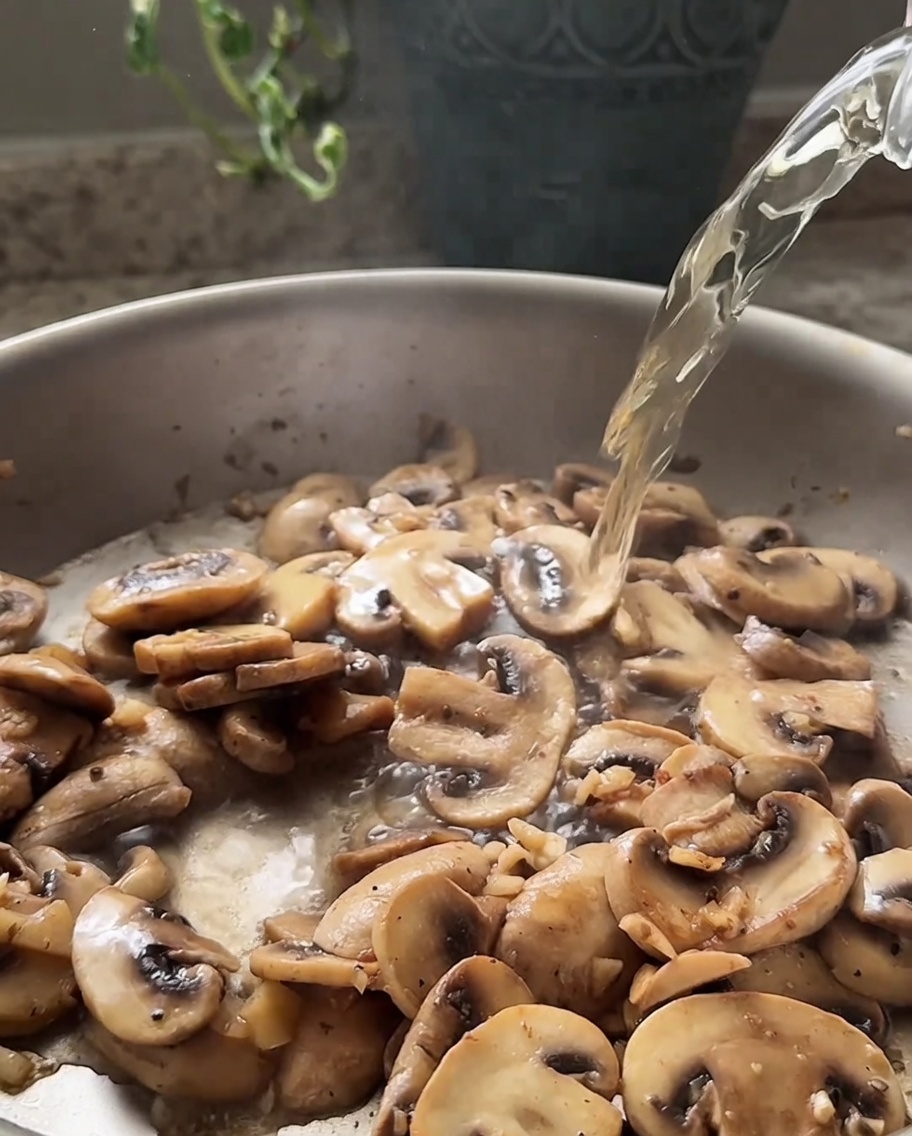 Vin blanc versé dun verre dans une poêle contenant des champignons émincés sautés.