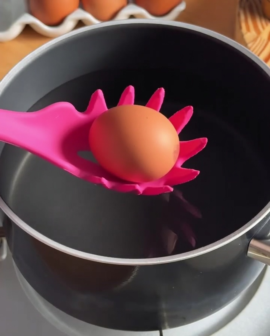 Un œuf plongé dans une casserole deau chaude à laide dune cuillère écumoire en silicone.