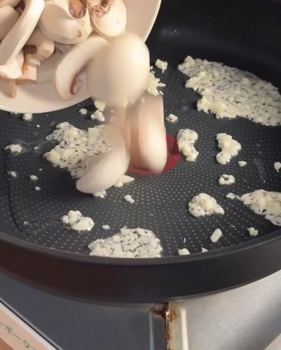 Tranches de champignons ajoutées dans la poêle avec lail sauté.