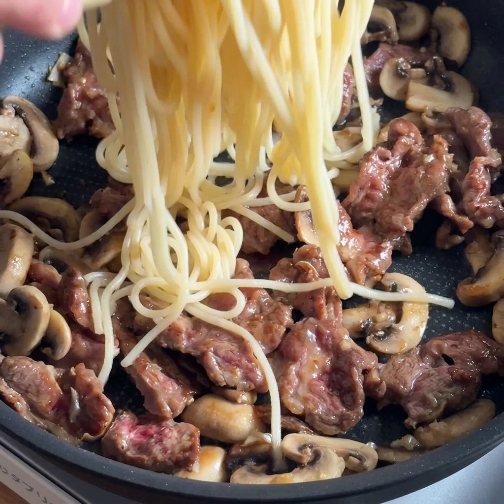 Pâtes ajoutées à la poêle avec le bœuf et les champignons, prêtes à être assaisonnées.