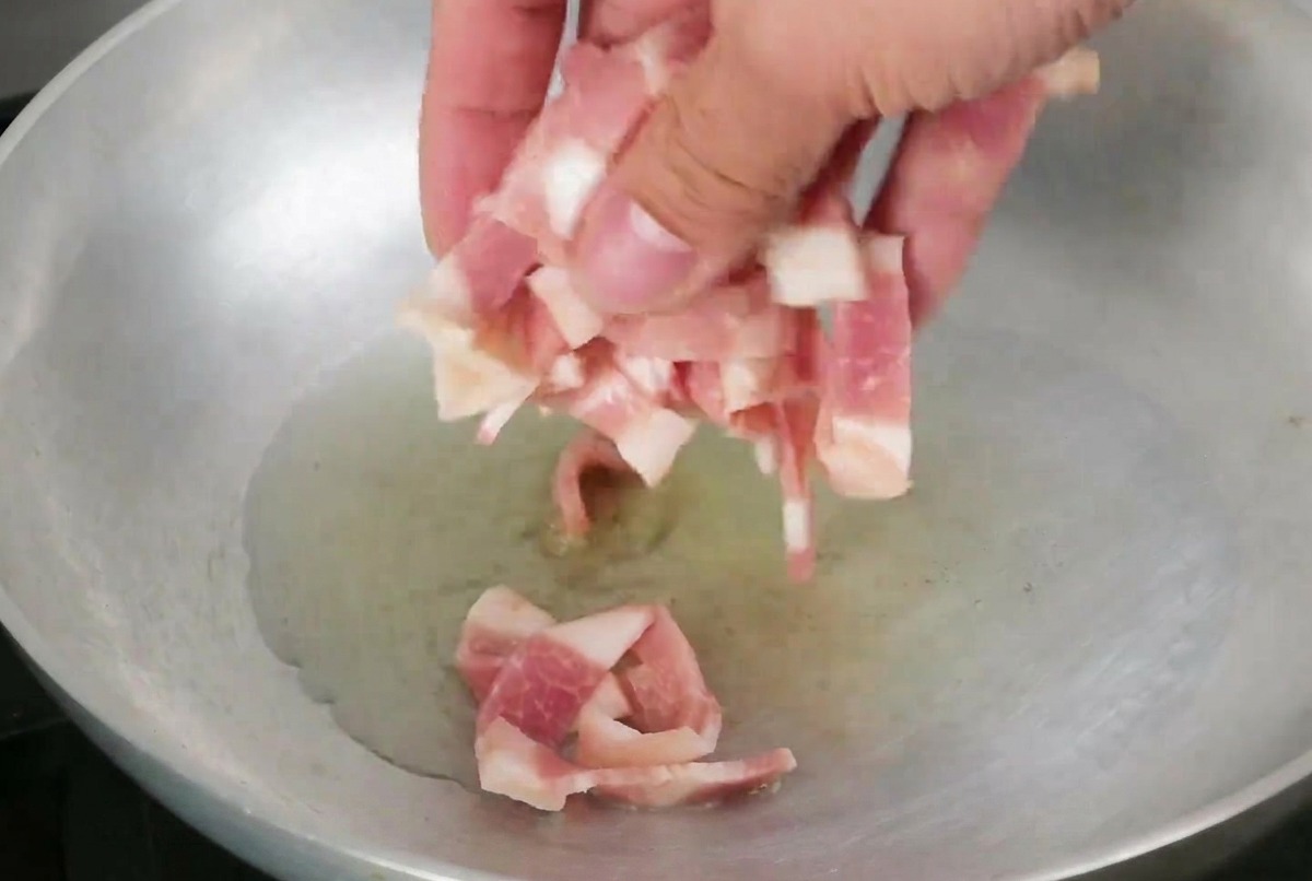Lardons en train de frire dans une poêle avec un filet dhuile dolive scintillante.