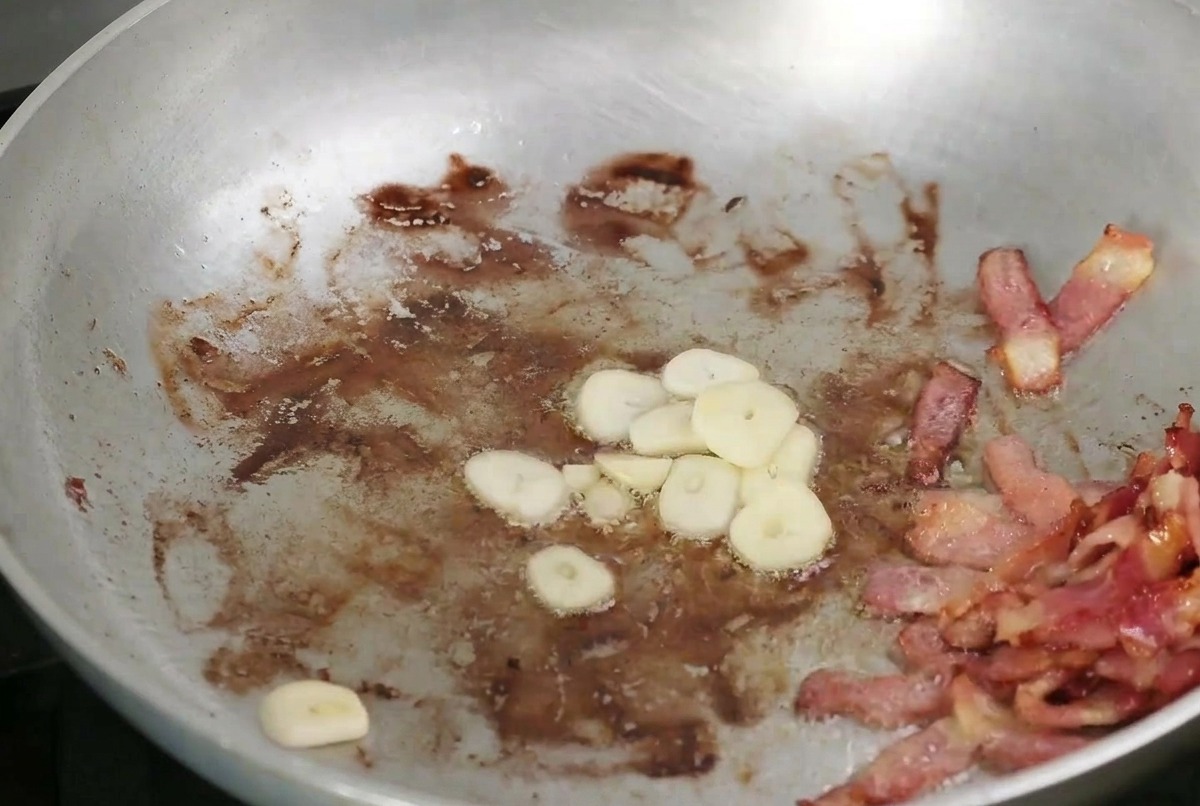 Ail émincé et champignons en train de dorer dans une poêle aux côtés du bacon croustillant.