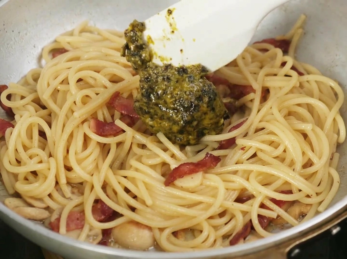 Une spatule mélangeant la sauce à la truffe noire aromatique dans une poêle de pâtes cuites, ail et bacon.