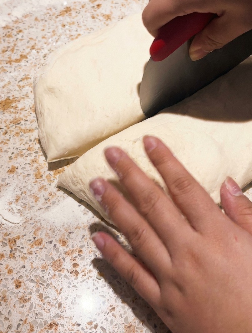 Une corne de pâtissier coupant un morceau de pâte à pizza fermentée sur un plan de travail.