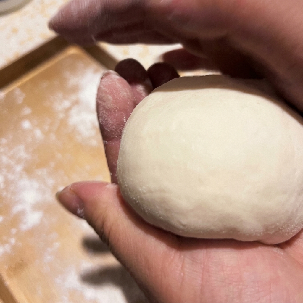 Des mains formant une boule de pâte à pizza lisse.