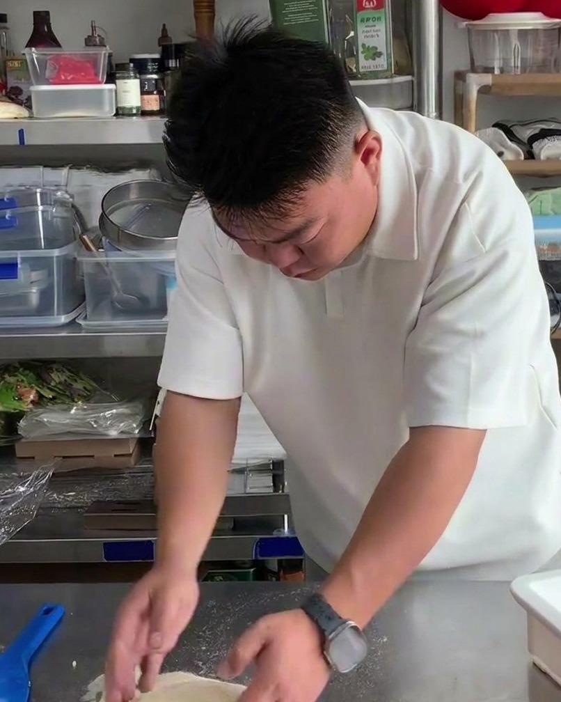 De la farine saupoudrée légèrement sur une boule de pâte à pizza crue sur une table en inox.