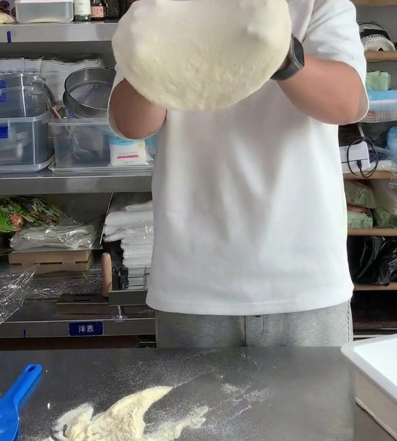 Pâte à pizza étirée sur les articulations des mains pour augmenter son diamètre et affiner le centre.