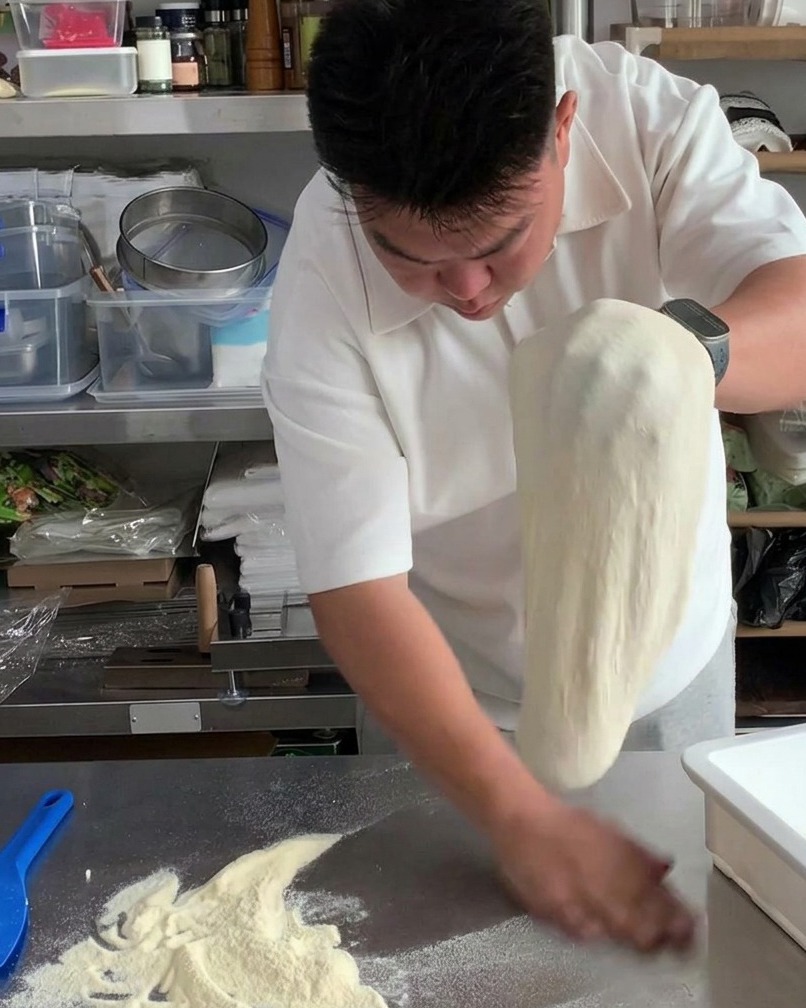 Des mains faisant passer la pâte étirée davant en arrière pour enlever lexcès de farine.