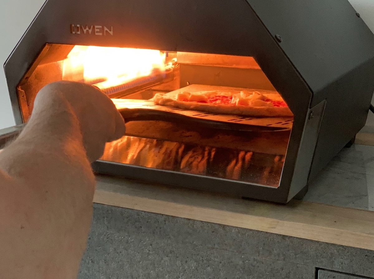 Une pelle à pizza glissant une pizza Margherita non cuite dans un four à pizza à gaz de table chaud.