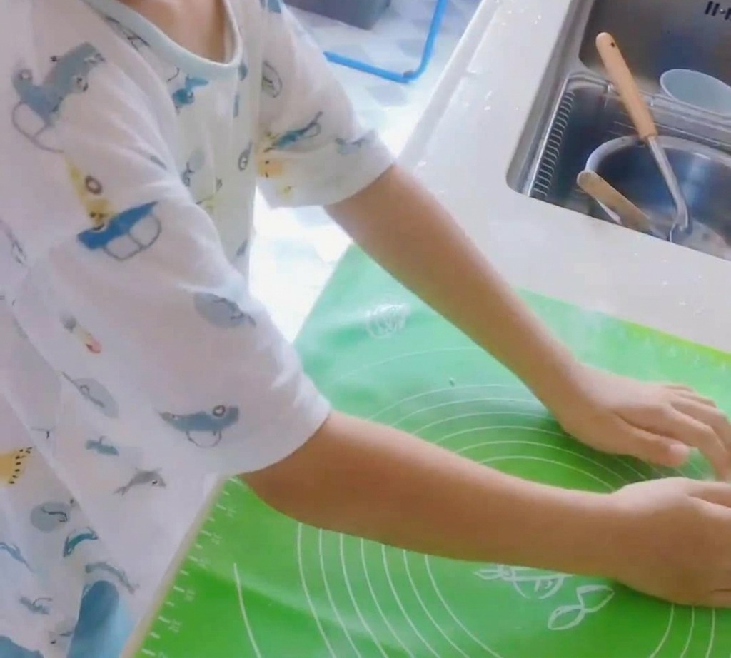 Une boule de pâte à pizza en cours de pétrissage sur un tapis en silicone vert.