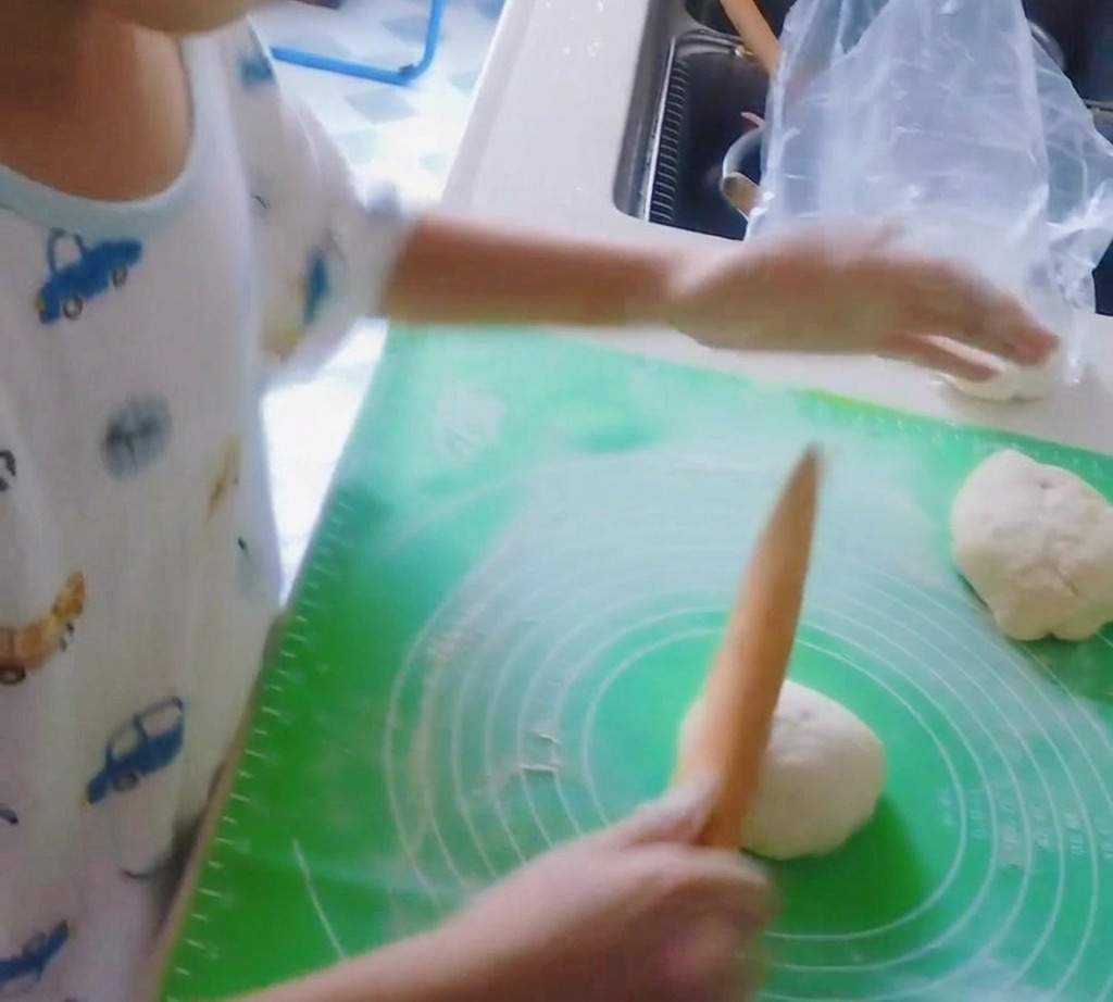 Un rouleau à pâtisserie en bois aplatissant une boule de pâte à pizza en un disque.