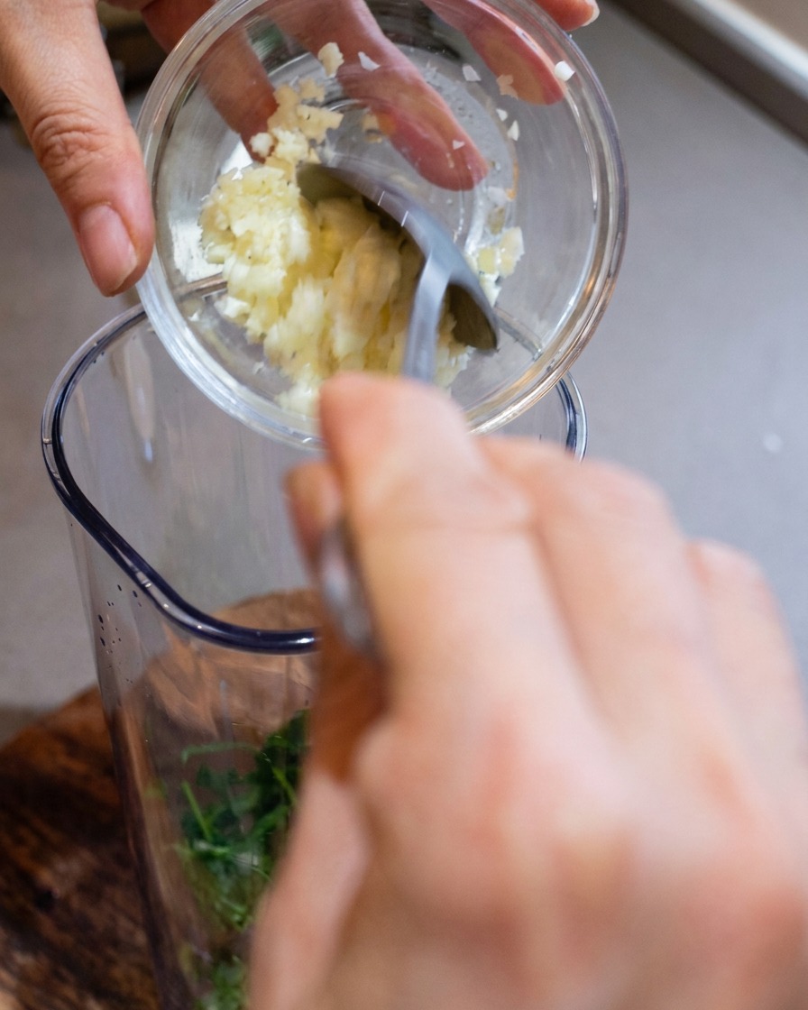 Un bol de mixeur rempli dail haché, de fromage fraîchement râpé et de pignons de pin grillés.