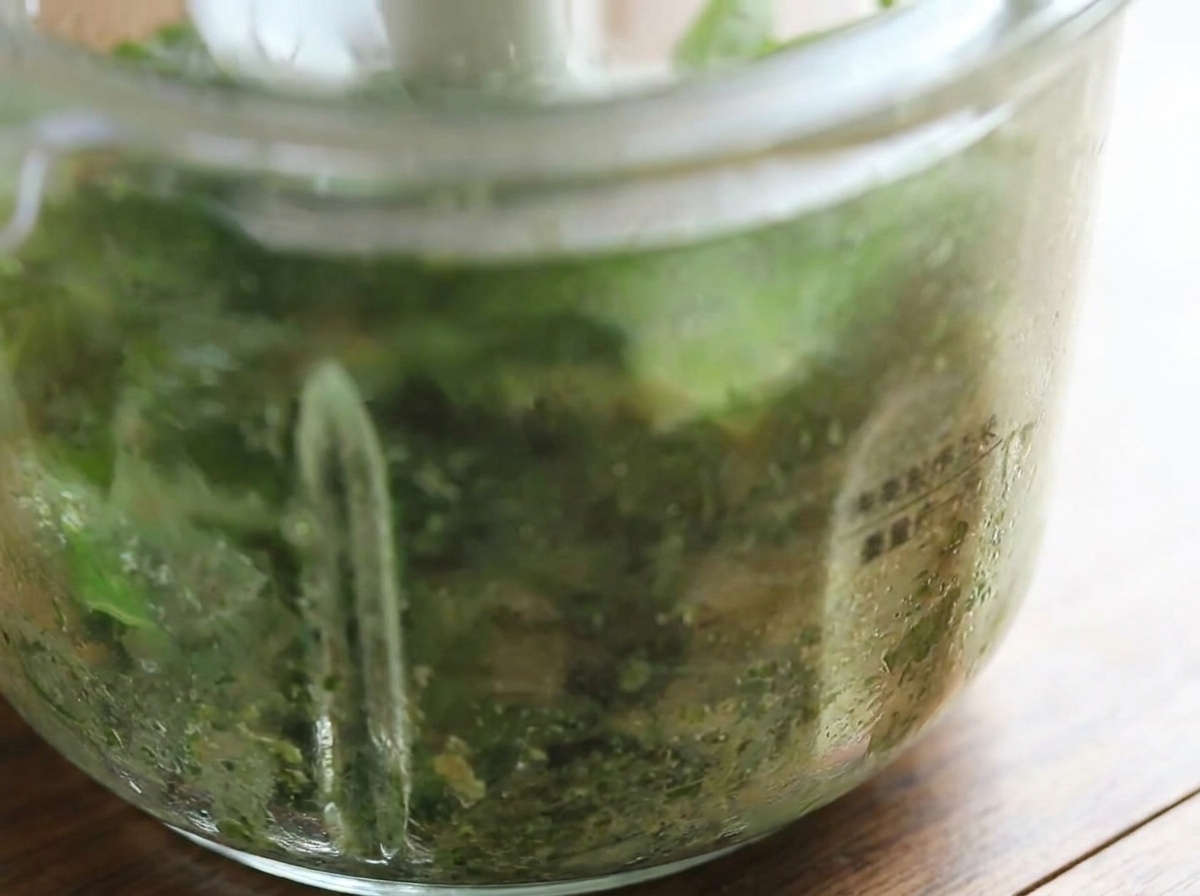 Gros plan sur le bol du robot culinaire montrant le pesto au basilic frais tout juste mixé dun vert éclatant.