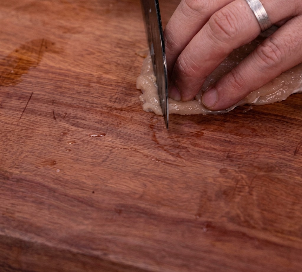 Blanc de poulet cru coupé en lamelles uniformes sur une planche à découper en bois.