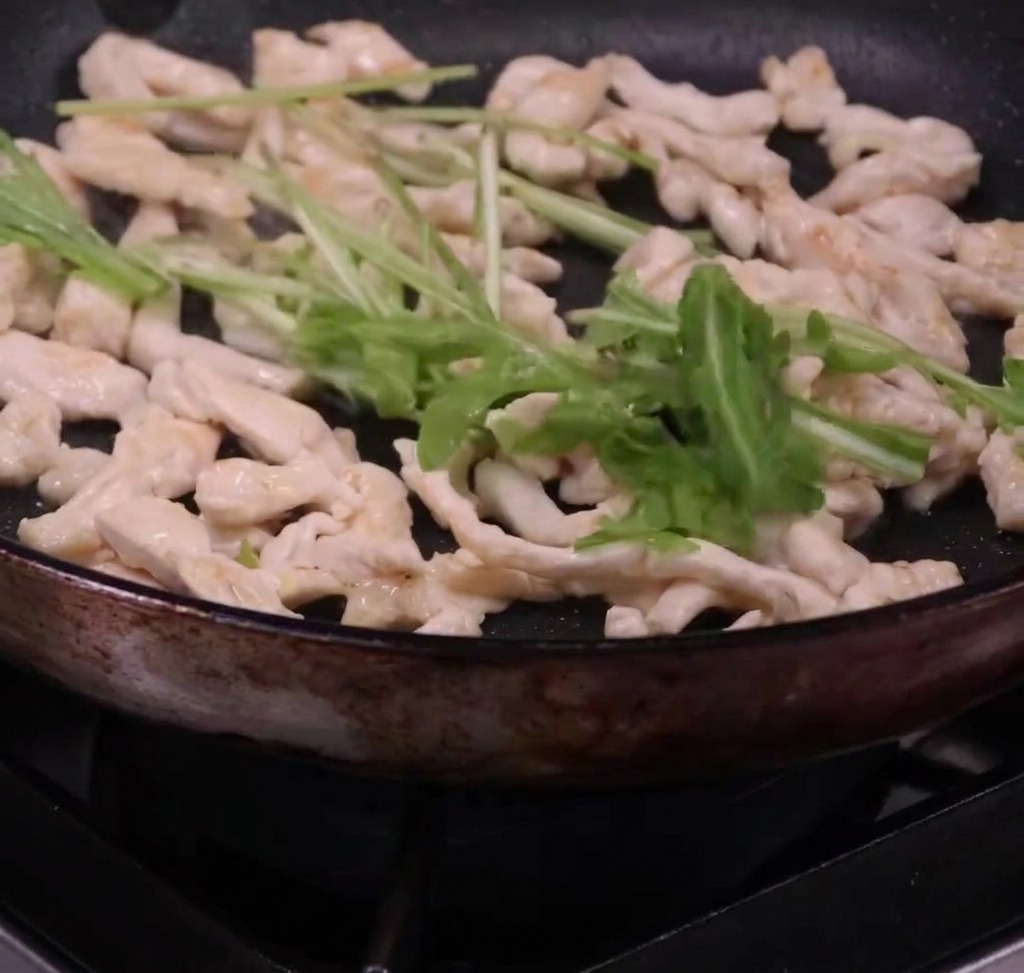 Spaghetti et roquette fraîche mélangés avec des lanières de poulet dans une poêle.