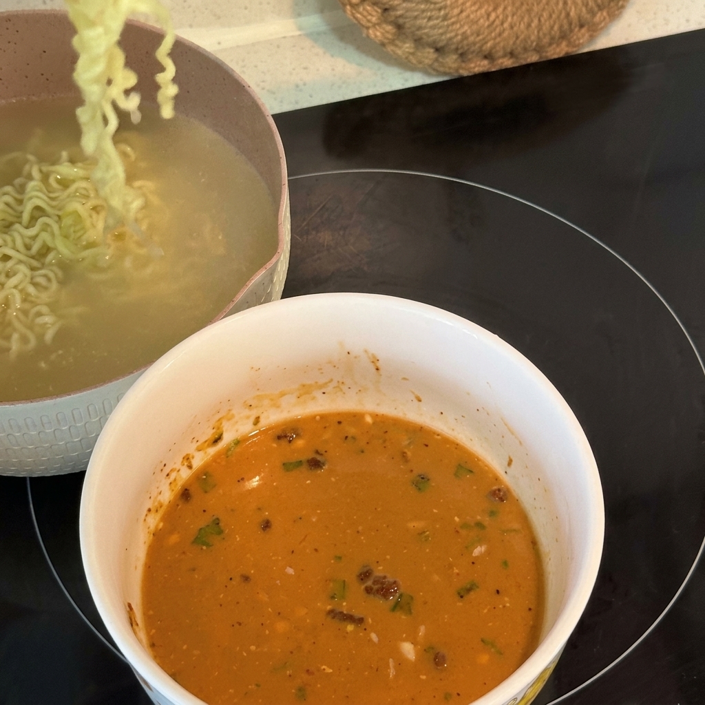 Des nouilles ramen frisées et cuites étant soulevées et transférées dans un bol rempli dune base de soupe crémeuse émulsionnée.