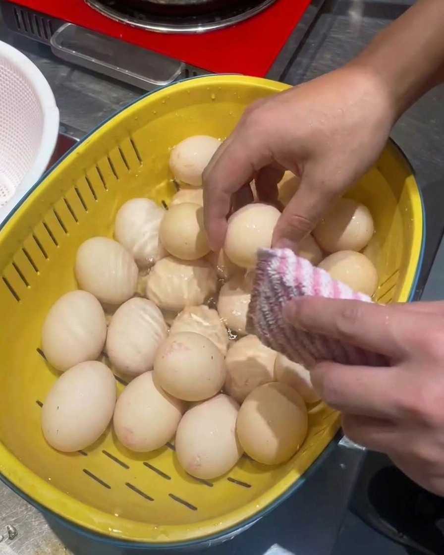 Œufs nettoyés dans une passoire jaune avec une éponge à récurer.