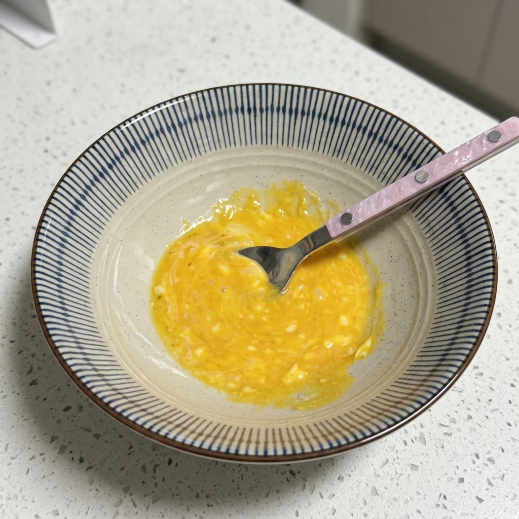 Un bol contenant une base de bouillon crémeuse jaune en train dêtre mélangée avec une cuillère.