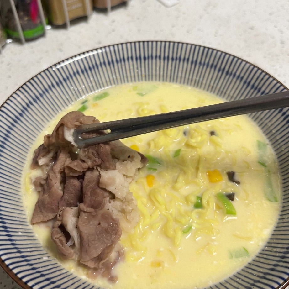 Une cuillerée de grains de maïs dorés saupoudrée sur un bol de ramen.