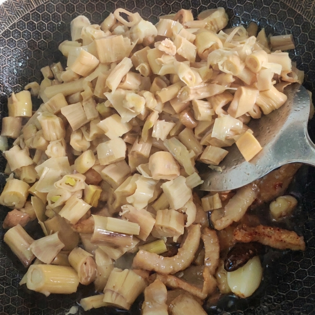 Ajout deau et de légumes moutarde marinés dans un wok rempli de porc et de bambou sautés.
