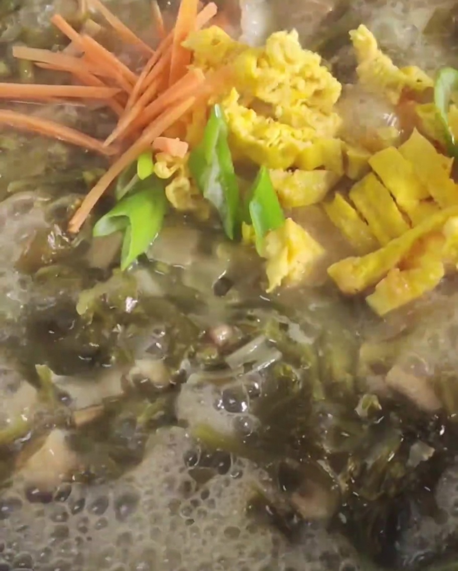 Ajout de carottes et dœuf frit tranché dans une marmite de bouillon bouillonnante.