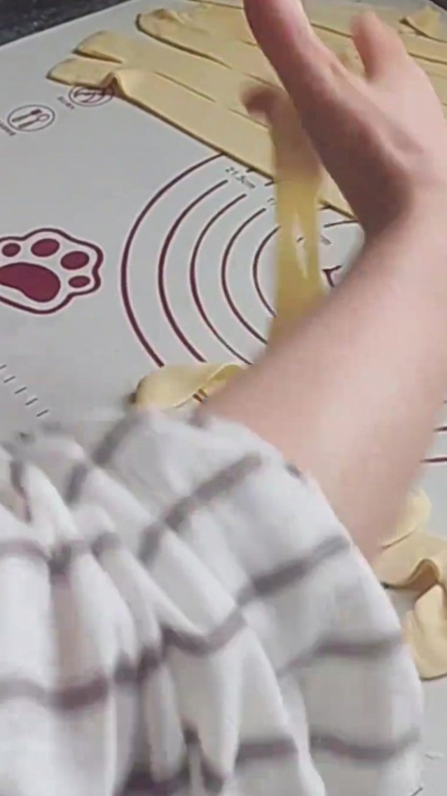 Des mains étirant un brin de pâte contre un tapis en silicone, le préparant à la cuisson.
