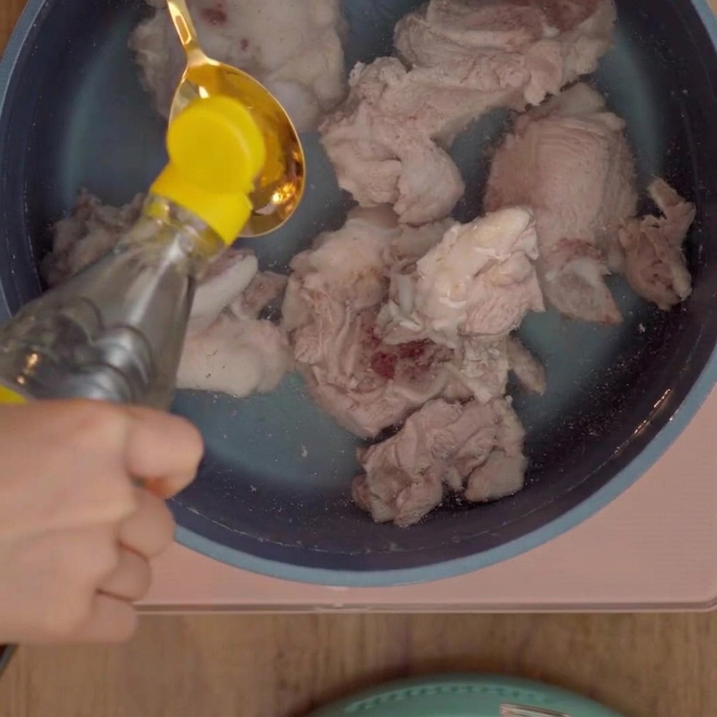 Une cuillère à soupe versant du vinaigre blanc dans une marmite dos de porc.