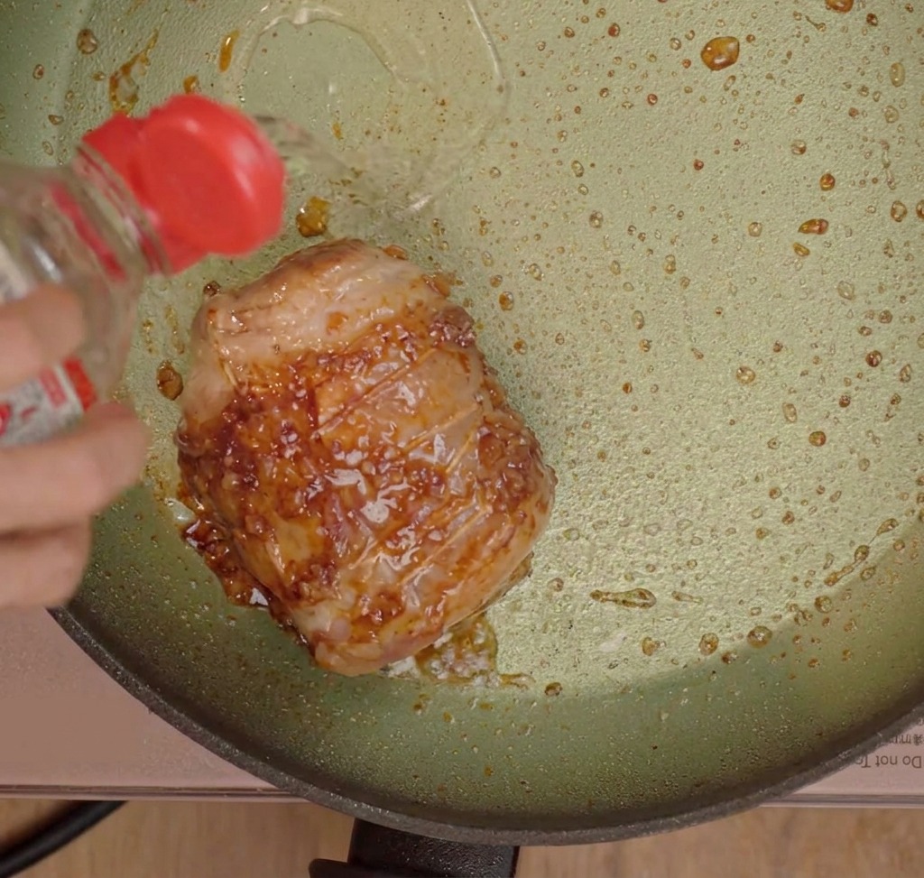 Assaisonnements liquides versés sur la poitrine de porc saisie dans une poêle.