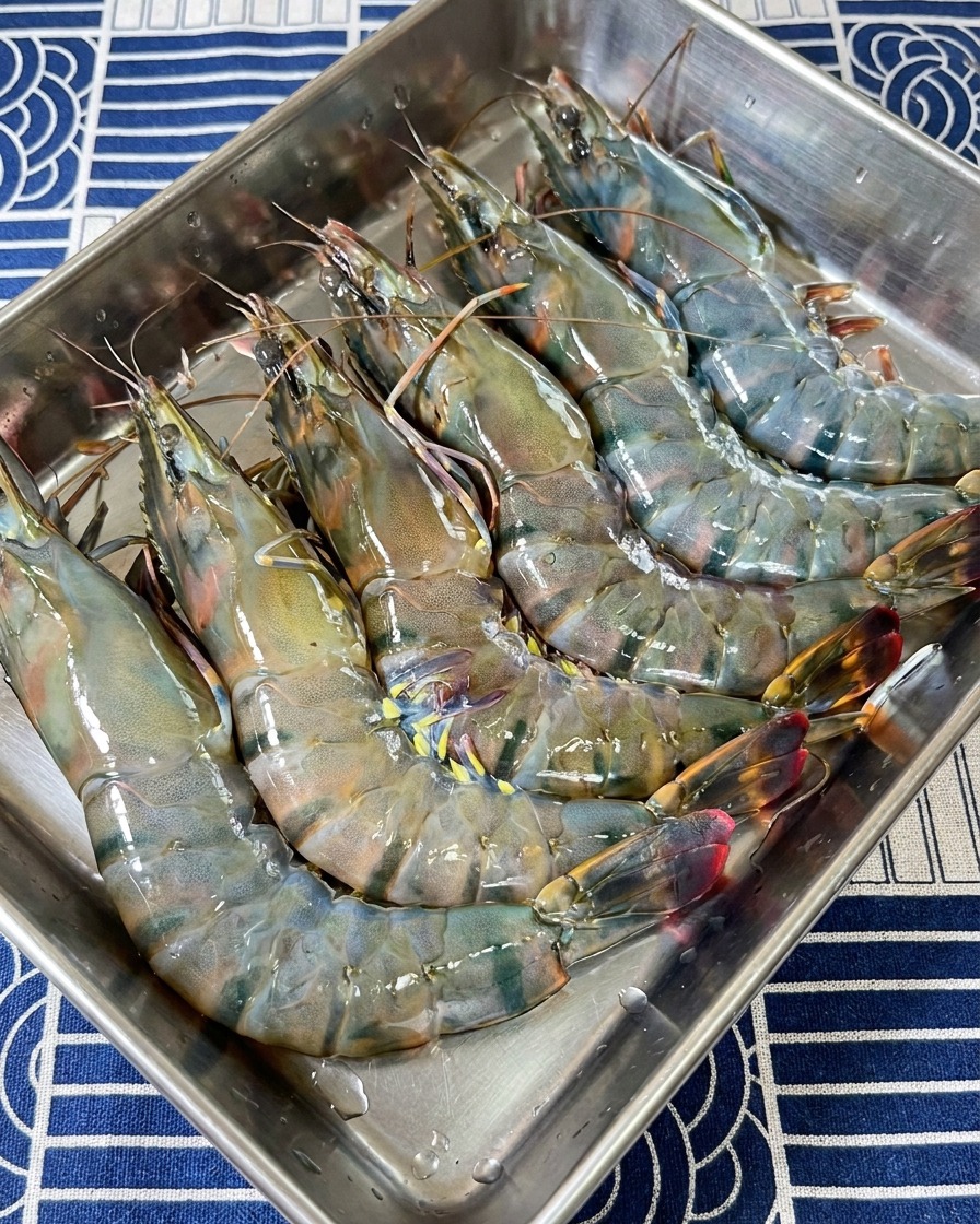 Collection de têtes et carapaces de crevettes tigrées crues dans un plateau de préparation en inox.