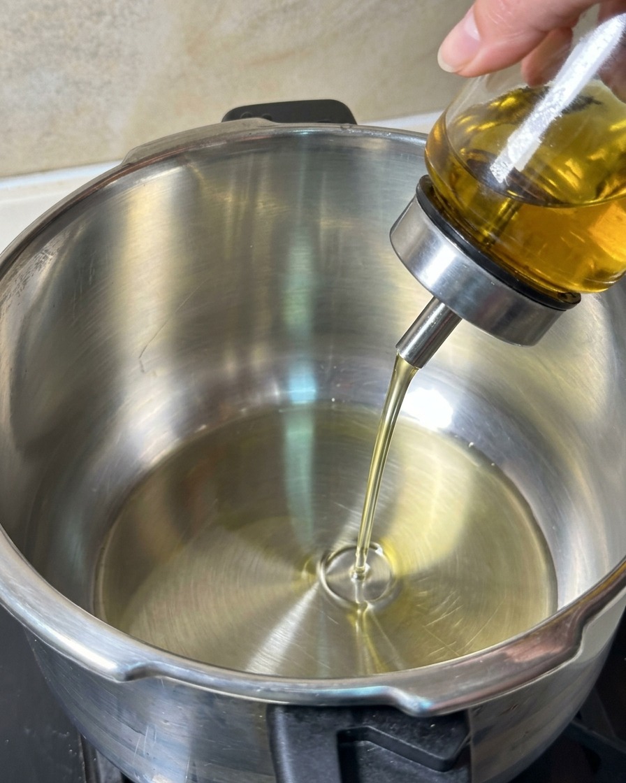 Huile de cuisson versée depuis un doseur en verre dans une casserole propre en inox.