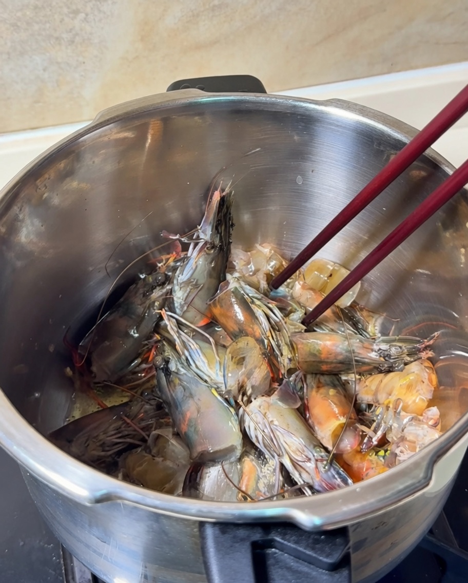 Têtes et carapaces de crevettes sautées dans une casserole, prenant une couleur orange vif.
