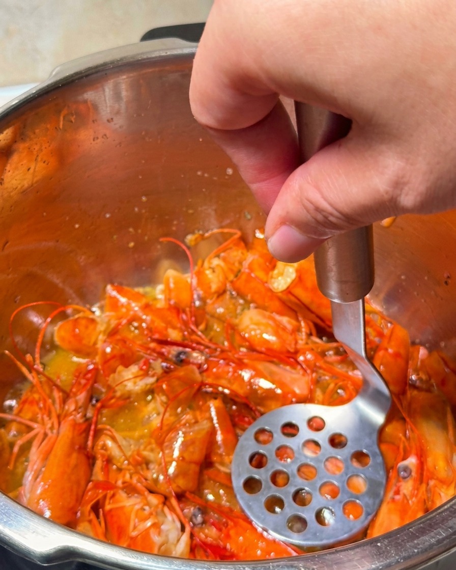 Un presse-purée écrasant les têtes de crevettes en train de frire pour extraire lhuile orange dorée.
