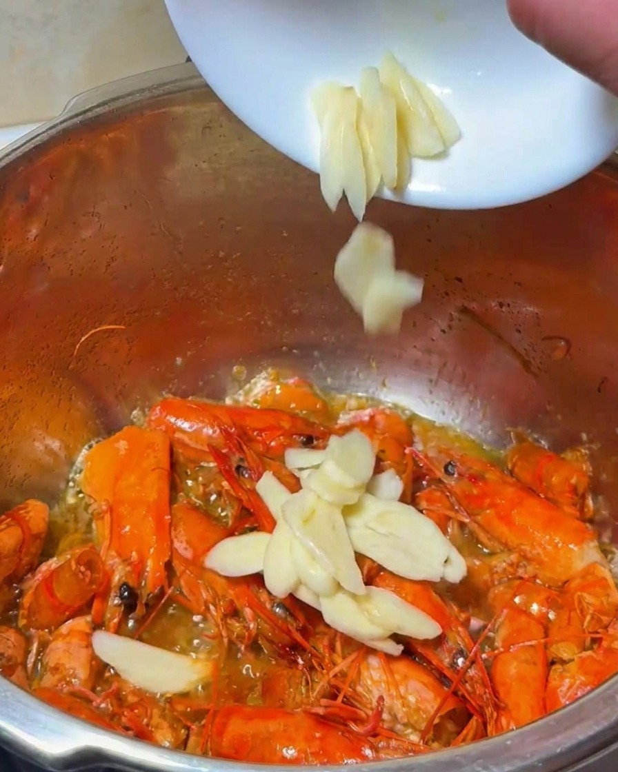 Ail et oignon tranchés ajoutés dans la casserole de carapaces de crevettes frites.