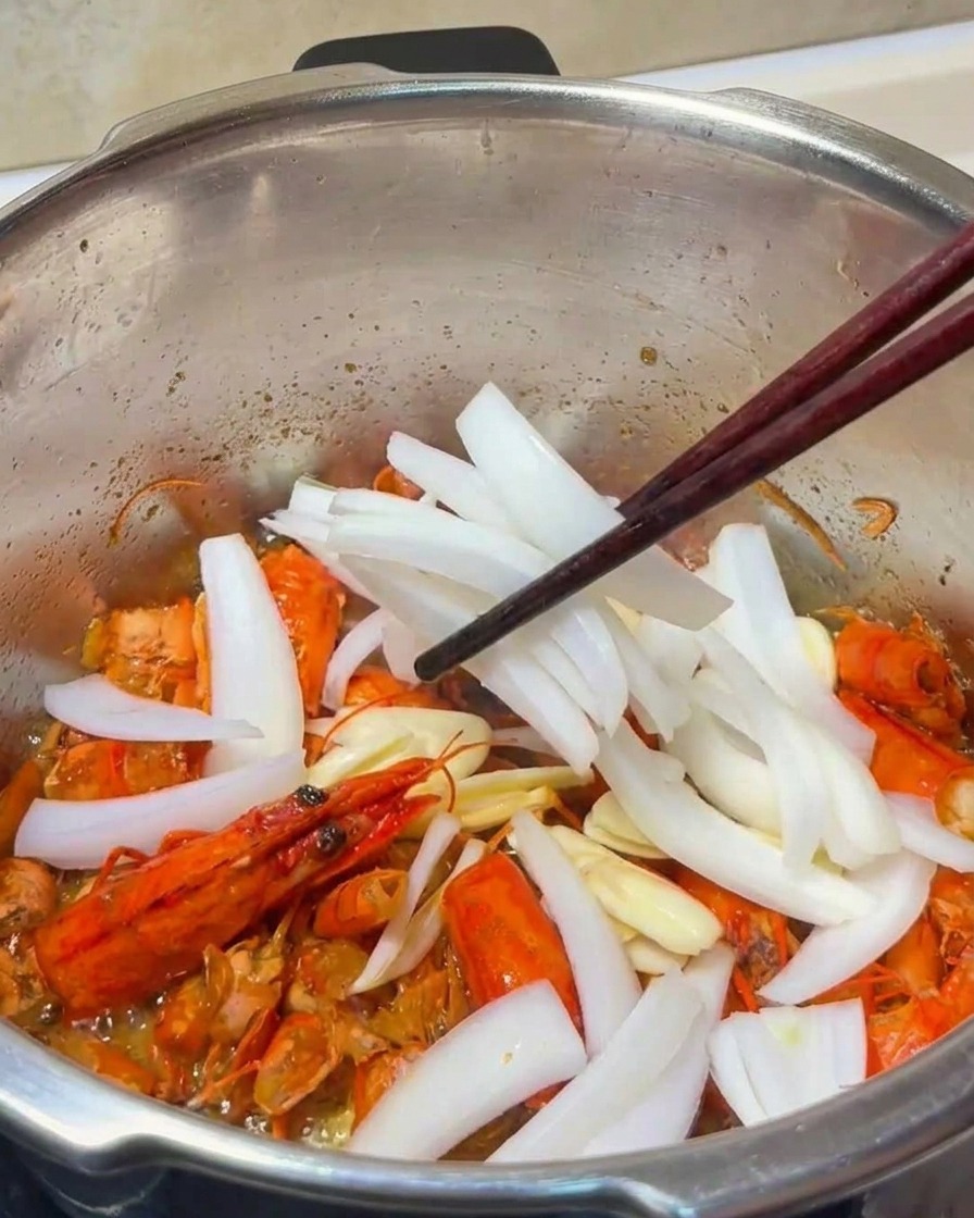 Gros plan sur des tranches dail et des lamelles doignon mélangées aux carapaces de crevettes frites dans une casserole en métal.