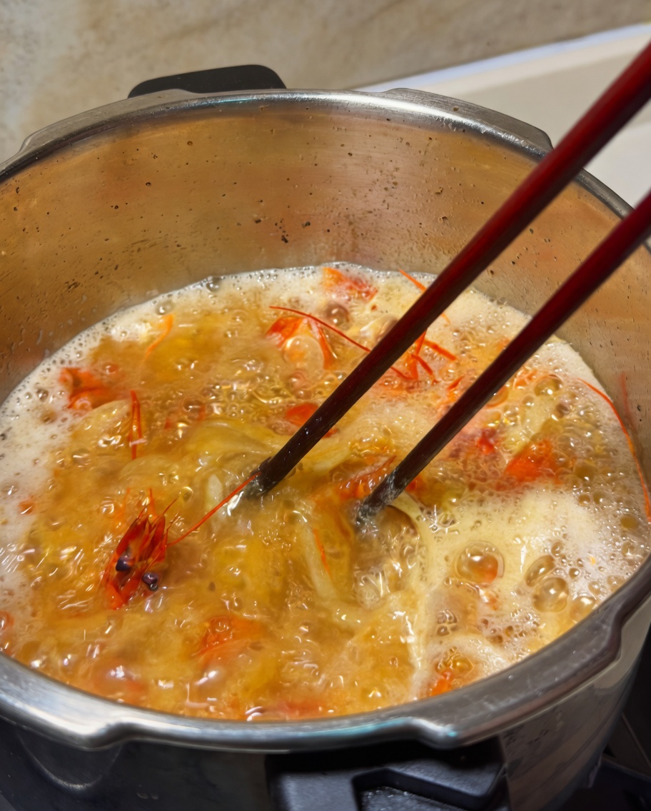 Une noisette de beurre fondant dans une casserole de bouillon de crevettes orange frémissant, remué avec des baguettes.