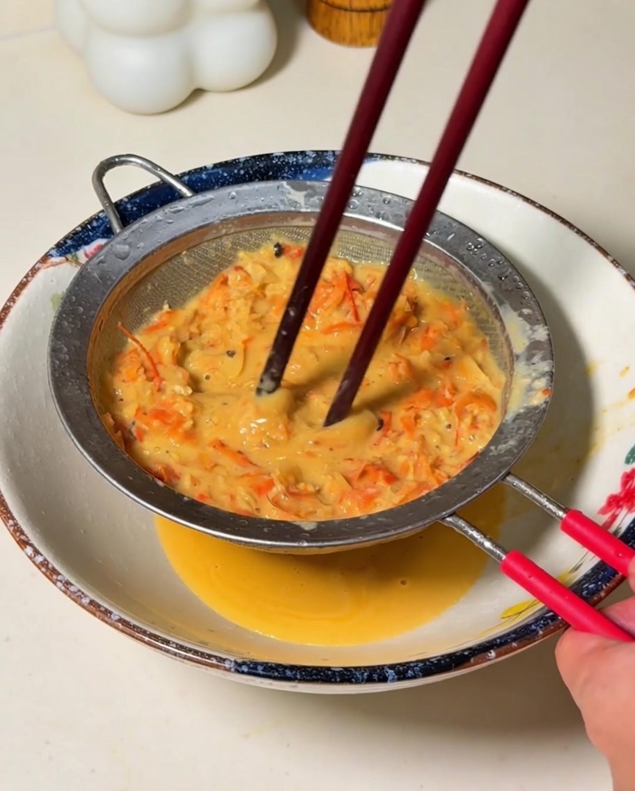 Le mélange orange mixé étant filtré à travers un tamis fin dans un bol, pressé par des baguettes.