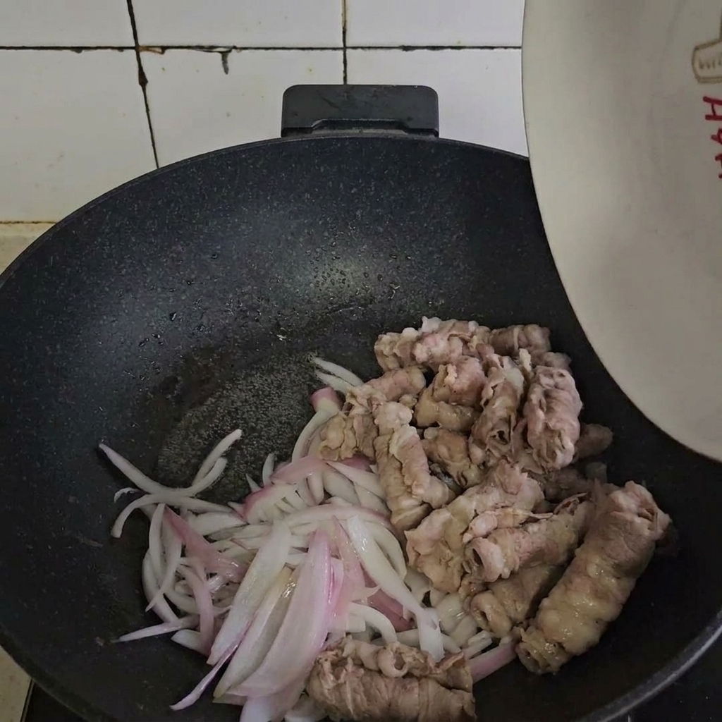 Tranches de bœuf blanchies incorporées aux oignons sautés dans une poêle chaude.