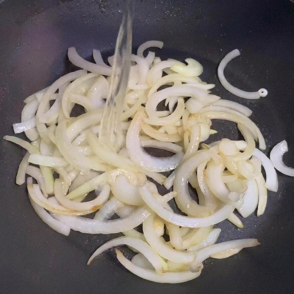 Du saké versé sur les oignons sautés dans une poêle.