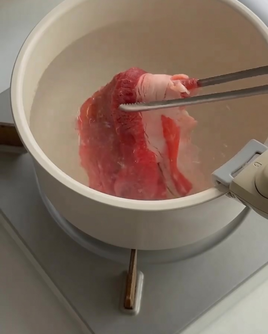 Fines tranches de bœuf cru plongées dans une casserole deau bouillante avec des pinces.